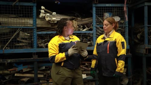 Deux ingénieures portant des équipements de sécurité inspectant l'inventaire des pièces automobiles dans un entrepôt industriel