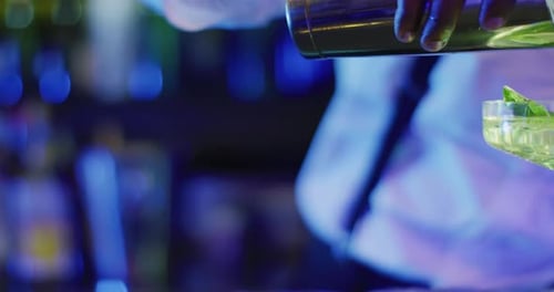 Video of midsection of african american barman preparing green cocktail at the bar