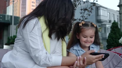Mother and Daughter Enjoy Time Together in the Park While Using a Smartphone