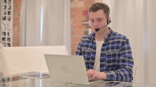 Young Casual Man with Headset Talking with Customers Online in Call Center