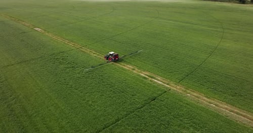tractor operating a continuous spray containing agrochemicals on a farm aerial shot