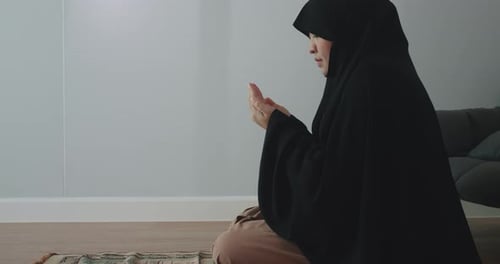 Eine asiatische muslimische Frau im schwarzen Hijab betet mit erhobenen Händen als Segen für Gott.