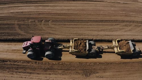 Luftaufnahme eines roten Traktors, der jede Menge Erde zieht und die Felder für die kommende Saison vorbereitet.