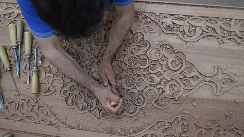 Man Carving Intricate Wood Design with Hand Tools