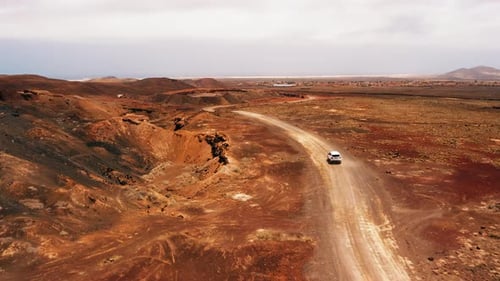 White Car Driving Alone Travel on Empty Dirt Road Freeway Through Desert Volcanic Landscape at