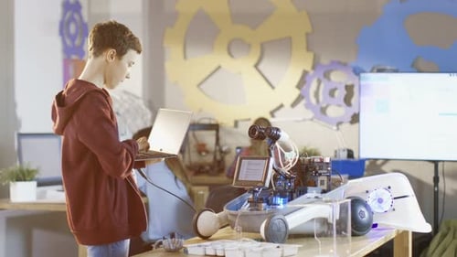 Smart Young Boy Programs Robot with a Laptop. He's Building Robot for His Science/ Robotics Class.