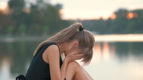 Woman Sitting by Lake Crying at Sunset
