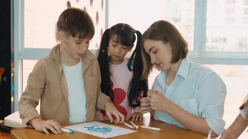 Children Coloring at Table with Teacher in Classroom