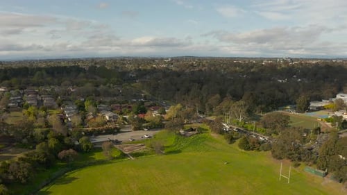 Aerial view smoothly tracks forward, revealing a parkland area and the flow of traffic on the nearby