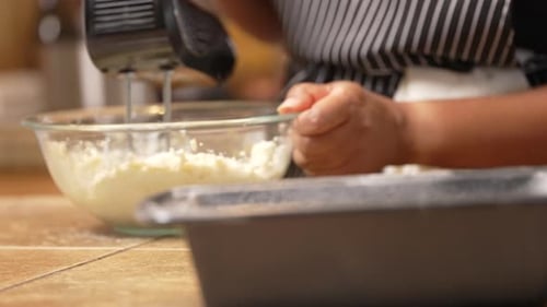 Homemaker mixing cake batter to bake in a bread pan - rack focus from the pan to the mixing bowl