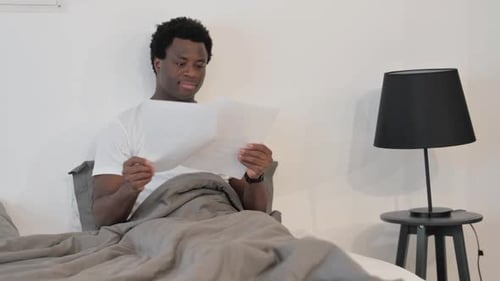 Man Sitting in Bed Reading a Paper