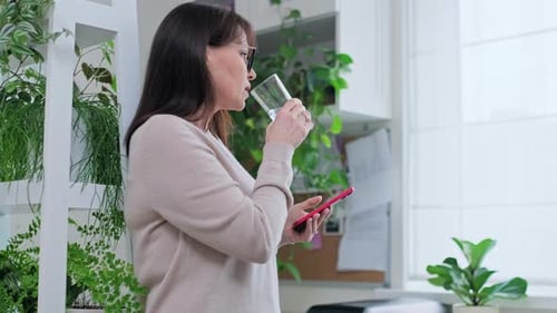 Woman Drinks Water While Using Mobile Phone