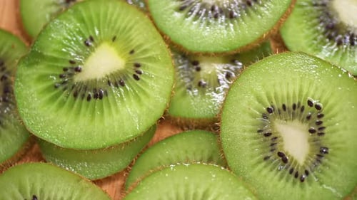 A close-up of fresh kiwi slices arranged on a wooden surface. The vibrant green color, black seeds,