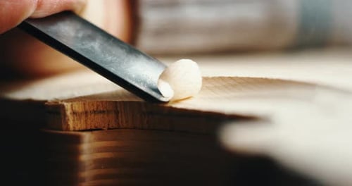 Macro au ralenti d'un maître artisan luthier effectuant un travail minutieux et détaillé sur un violon en bois dans un atelier