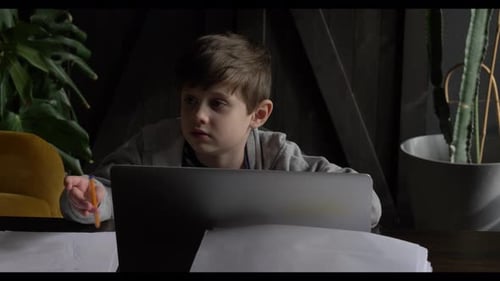 Ein junger Junge im Schulalter sitzt zu Hause am Schreibtisch seines Vaters, umgeben von einem Laptop und Dokumenten