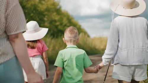Woman Holding Son Hand While Walking Alongside Girl in Pink on Dirt Path