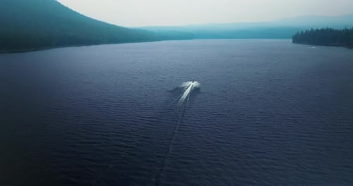 Aerial rear view follows speed boat wake across open deep blue mountainous lake