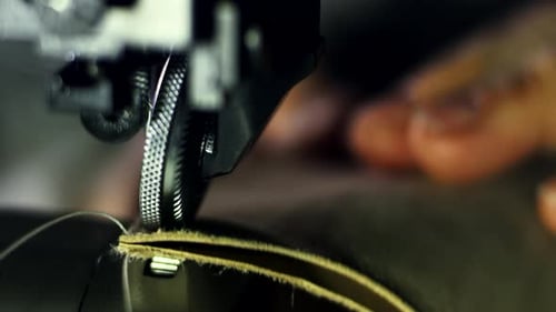 Craftsman hands stitching leather workpieces together in a leather workshop