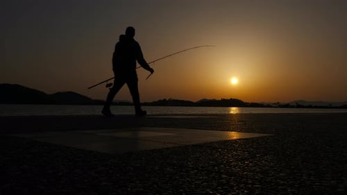 Pescador com uma vara de pescar ao pôr do sol