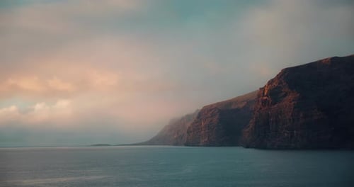 Ocean Dark Waters on Rocky Beach with Calm Waves at Sunset Cloudy Sky in Los Gigantes Cliffs
