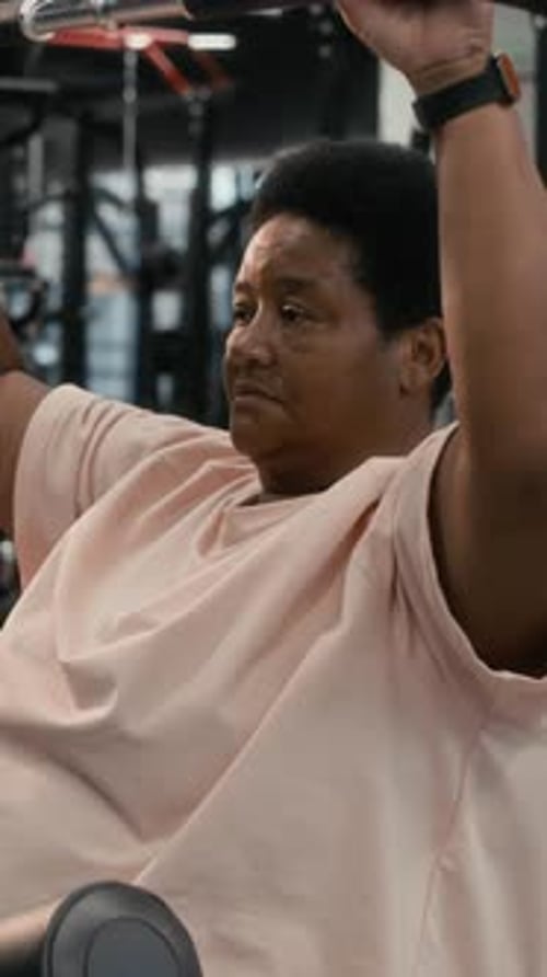 Vertical of Focused Senior Black Woman Using Lat Pulldown Machine in Gym