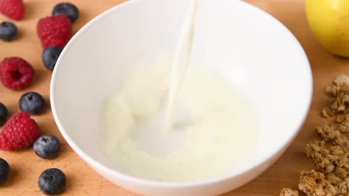 Pouring Milk into a Breakfast Bowl with Berries