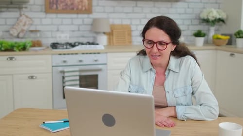 Woman Waving During a Laptop Video Call in Kitchen