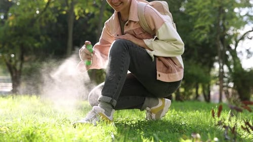 Woman spraying tick repellent onto leg in park, closeup