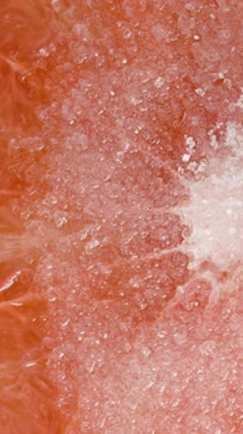 Vertical video. White sugar crystals quickly dissolve on the flesh of a red grapefruit. Macro.