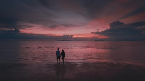 Man and Woman in Love Holding Hands Watching Beautiful Tropical Sunset Together Standing on Beach