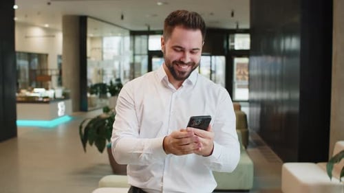 Happy Young Businessman Using Smartphone Shocked By Sudden Victory Lottery Win in Office Lobby