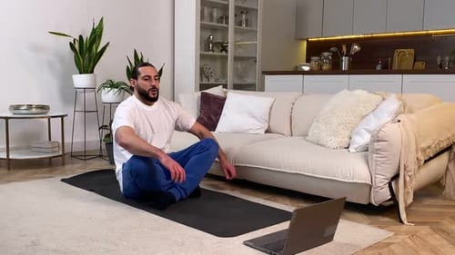 Hombre meditando siguiendo clases de yoga en línea a través de una computadora en interiores