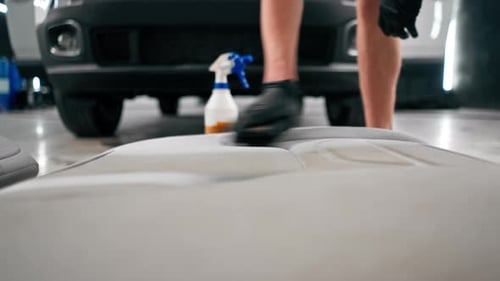 A close-up of a car wash worker using a vacuum cleaner to clean white car seats of detangling