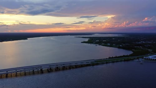 Bridge along wide river under colorful sunset sky aerial panorama