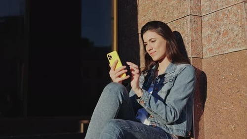Attractive Young Woman Using Her Smartphone for Messaging with Her Friend While Walking in City