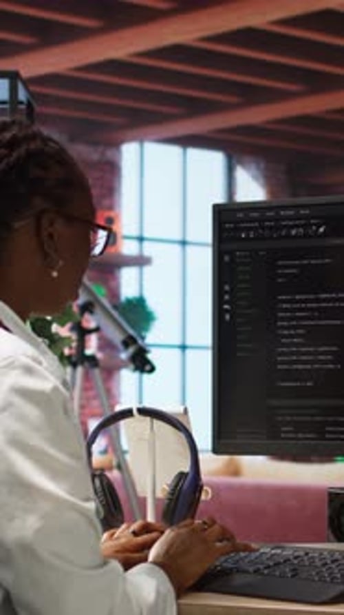 Woman works at computer with headphones in office