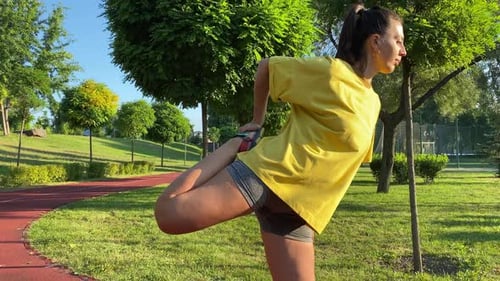 Young woman warms up exercising in golden sunlight of new day in park