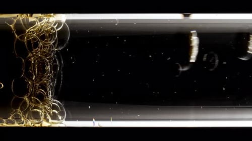 Foto macro de bolhas douradas de diferentes tamanhos descendo em tubo de ensaio de vidro sobre fundo preto