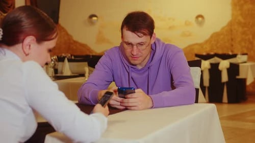Young Man and Woman Browsing Mobile Phone Sitting in Restaurant