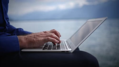 Man Typing on Laptop Computer by Lake