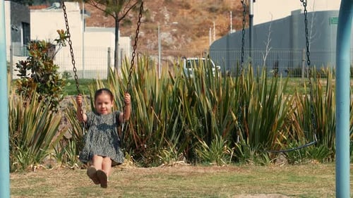 Happy cheerful happy smiling girl enjoying and playing on the swings of an outdoor playground