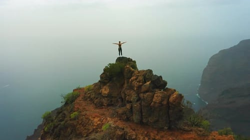 Woman Stands Atop Mountain Peak with Arms Outstretched