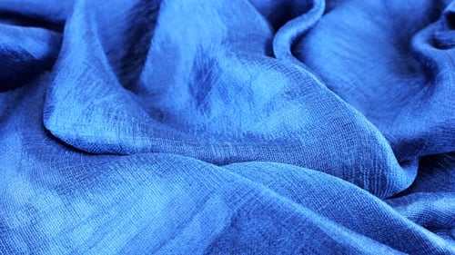 Close-up view of soft folds of dark blue silk muslin rotated on the display case. Textile background