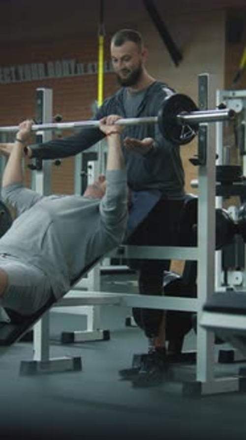 Athletic Man with Prosthetic Leg Exercises with Barbell in Gym with Personal Coach