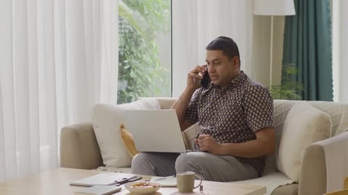 Businessman Calling on Phone when Working on Laptop at Home Office
