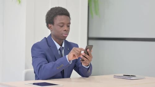 African Businessman Browsing Internet on Smartphone in Office