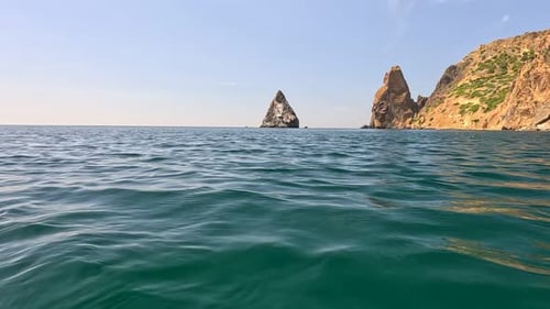 Sea Water Surface Camera Flies Over the Calm Azure Sea with Volcanic Rocky Shores on Background