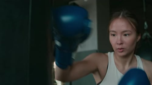 Young Asian Female Muay Thai Fighter Training with Punch Bag at Gym
