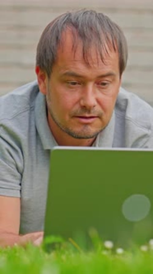 Mann, Freelancer, arbeitet draußen am Laptop, liegt im Park, Telearbeit, freiberuflicher Lebensstil