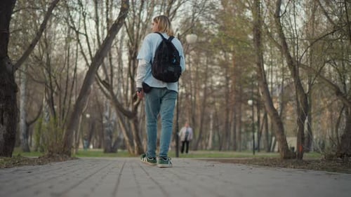 Teen walks down paved path in urban park
